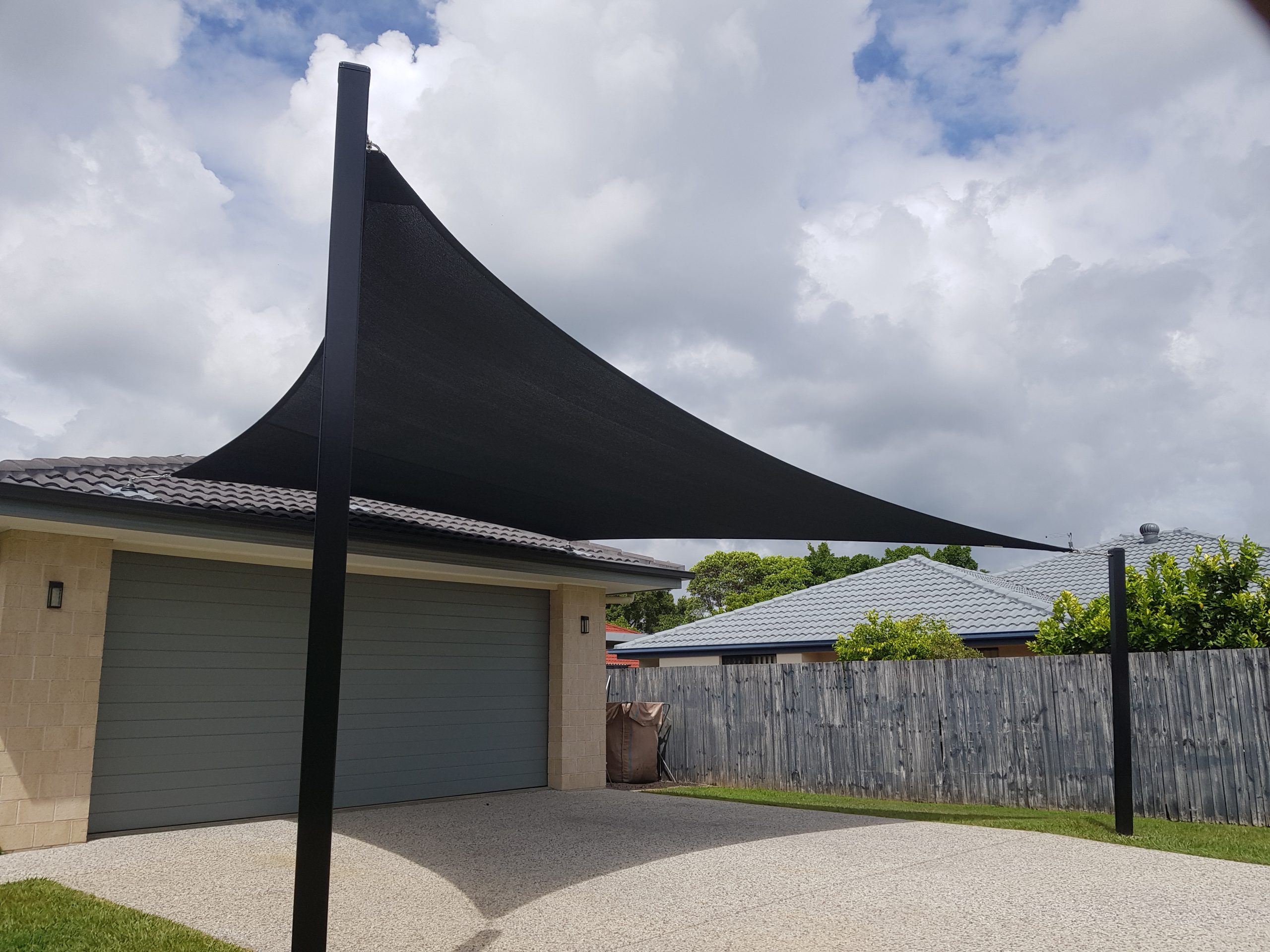 Modern house with a black car shade sail over the driveway, featuring a double garage and a grey fence in the background